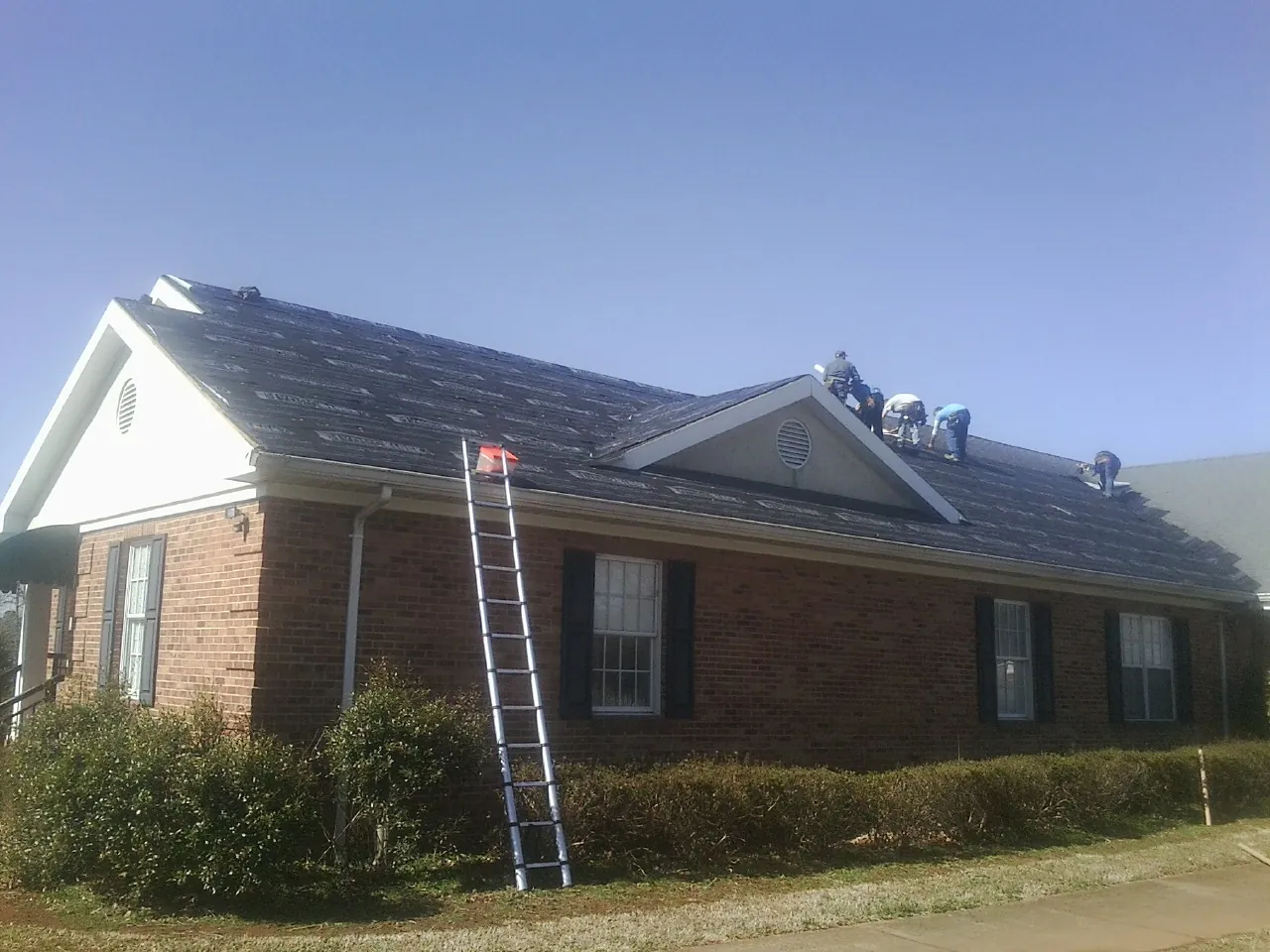 Crew tearing shingles off a brick ranch roof with a ladder set — Metal Roof Repair work by our crew in Yellow Springs
