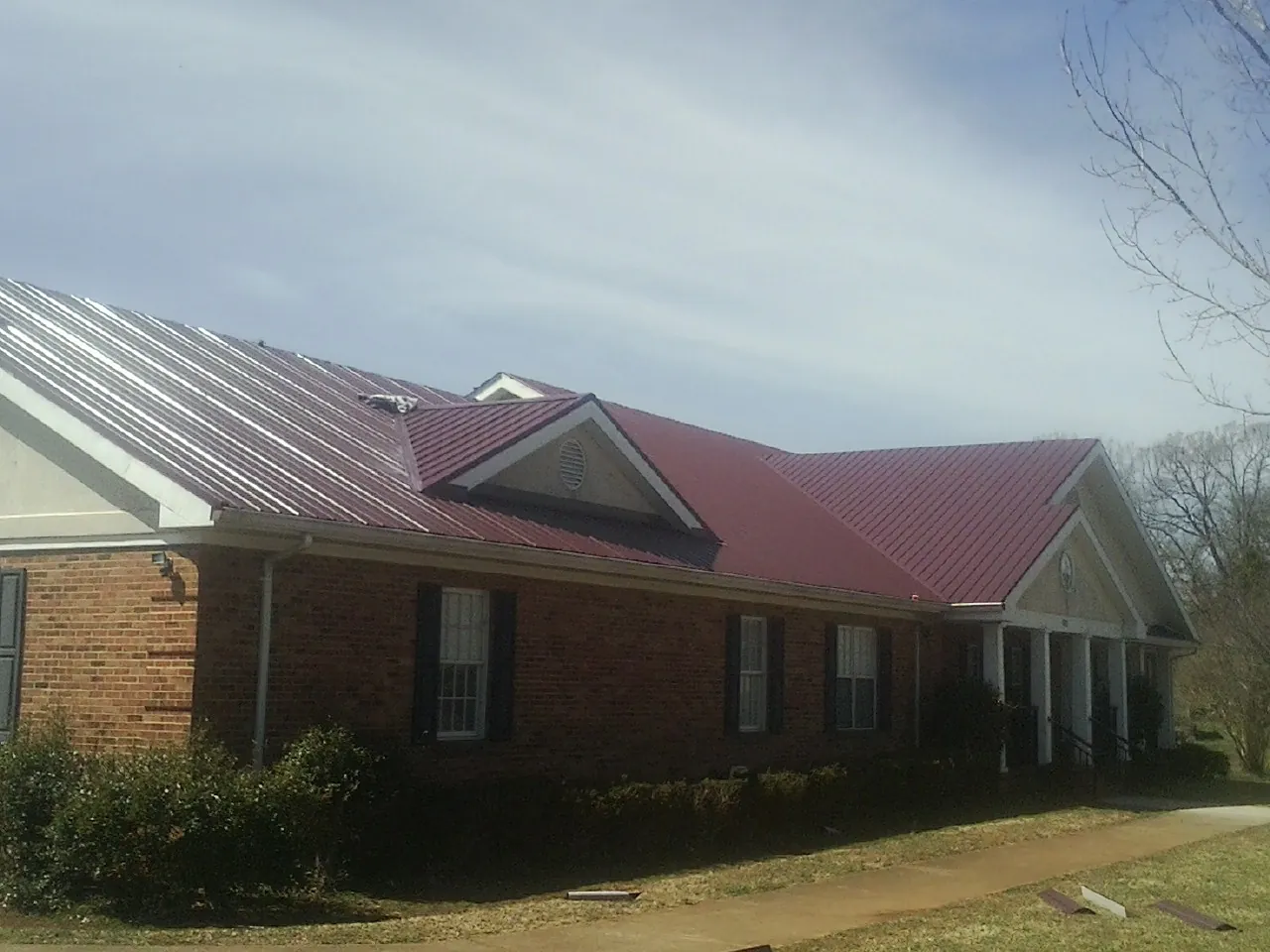 Red metal roof with gabled entries on a long brick building, from a Hail Damage Roof Repair job in Yellow Springs