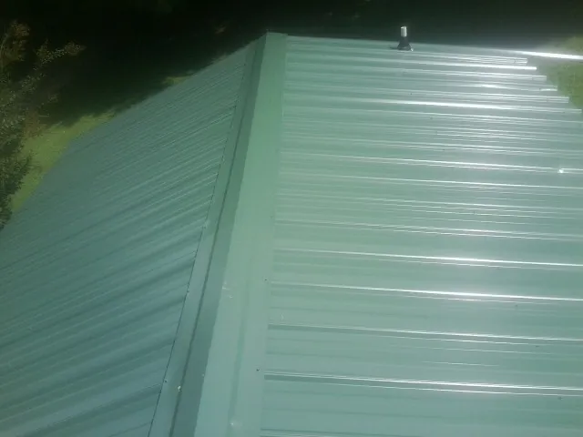 New green metal panels meeting at the ridge of a roof — Flat Roof Repair work by our crew in Yellow Springs