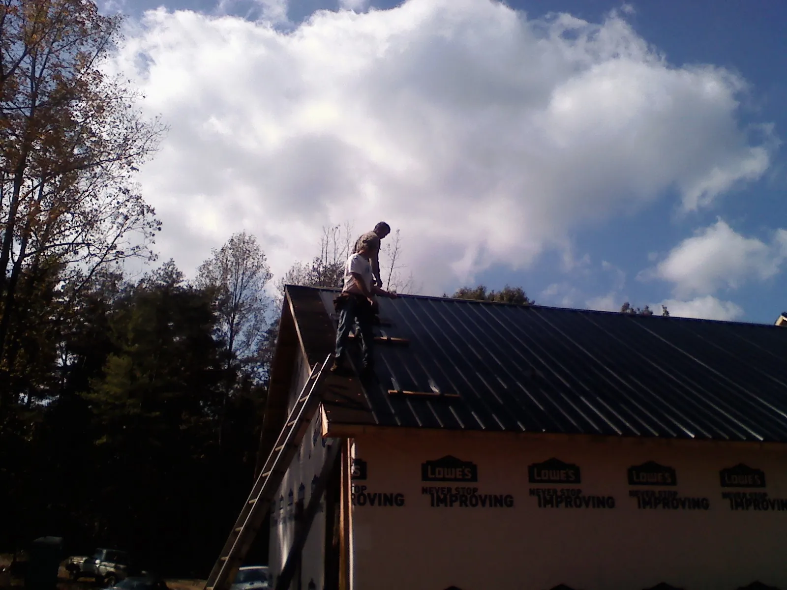 Roofer fastening dark metal panels high against a cloudy sky, from a Roof Inspection job in Yellow Springs