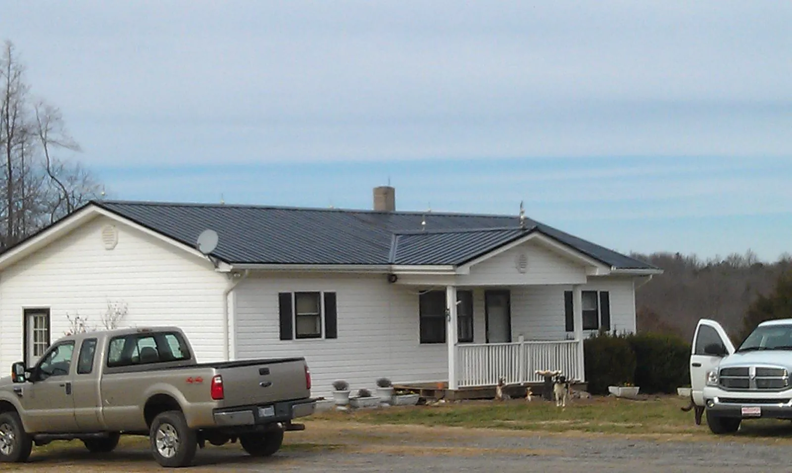 Finished dark metal roof on a white ranch home with work trucks parked in Yellow Springs