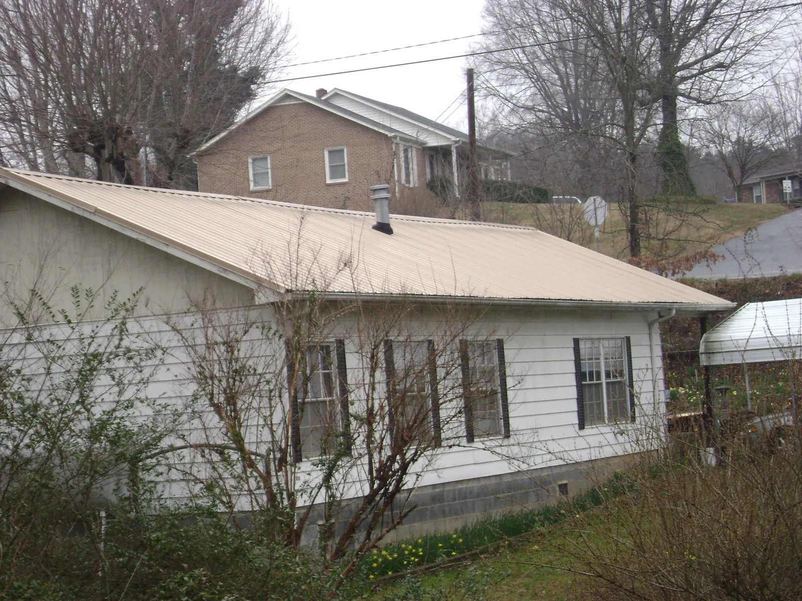 Tan metal roof on a white sided house set into a hillside — Commercial Roofing by Roofing Brothers in Yellow Springs